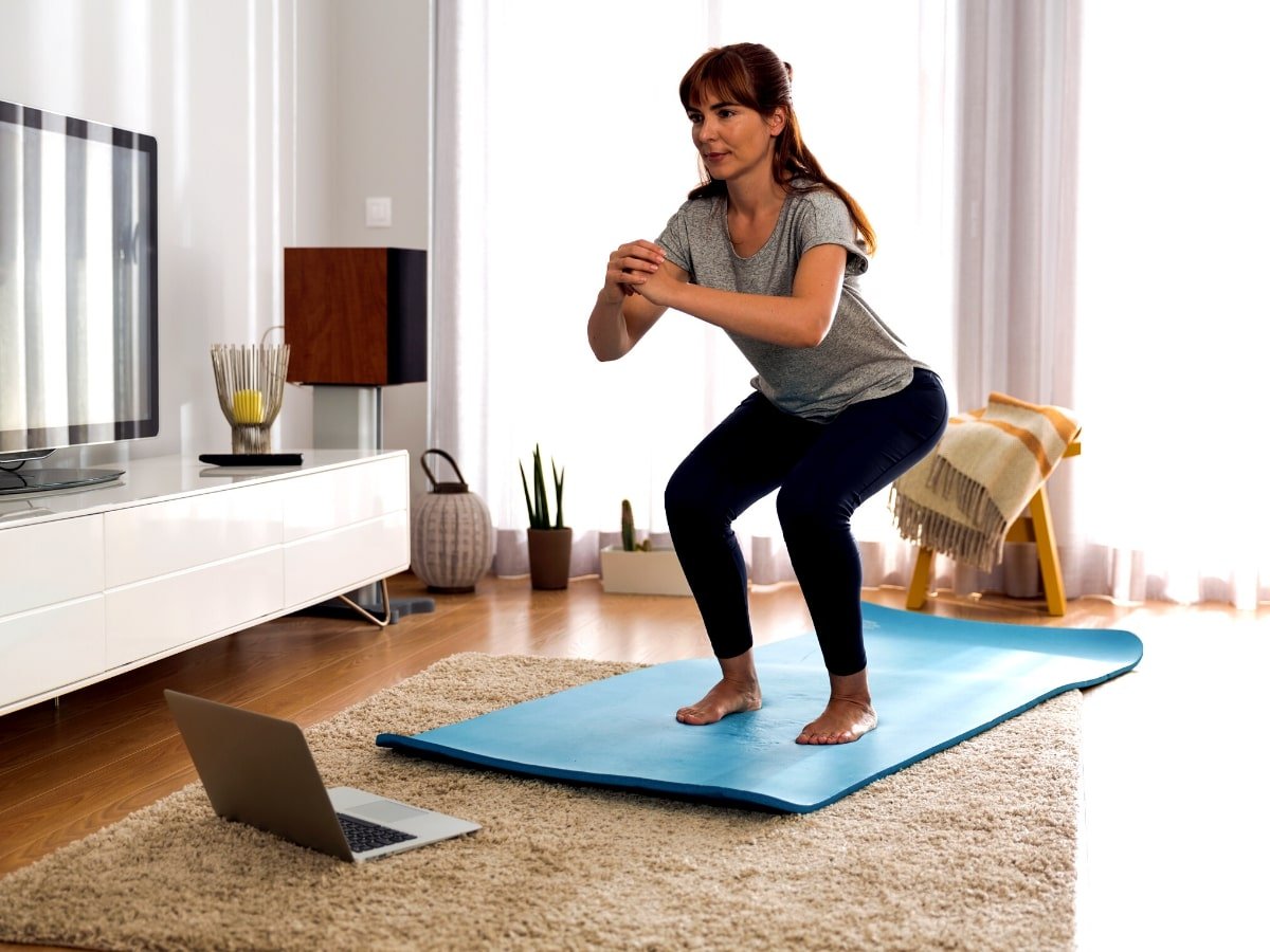 Woman doing a squat on a yoga mat in front of a laptop