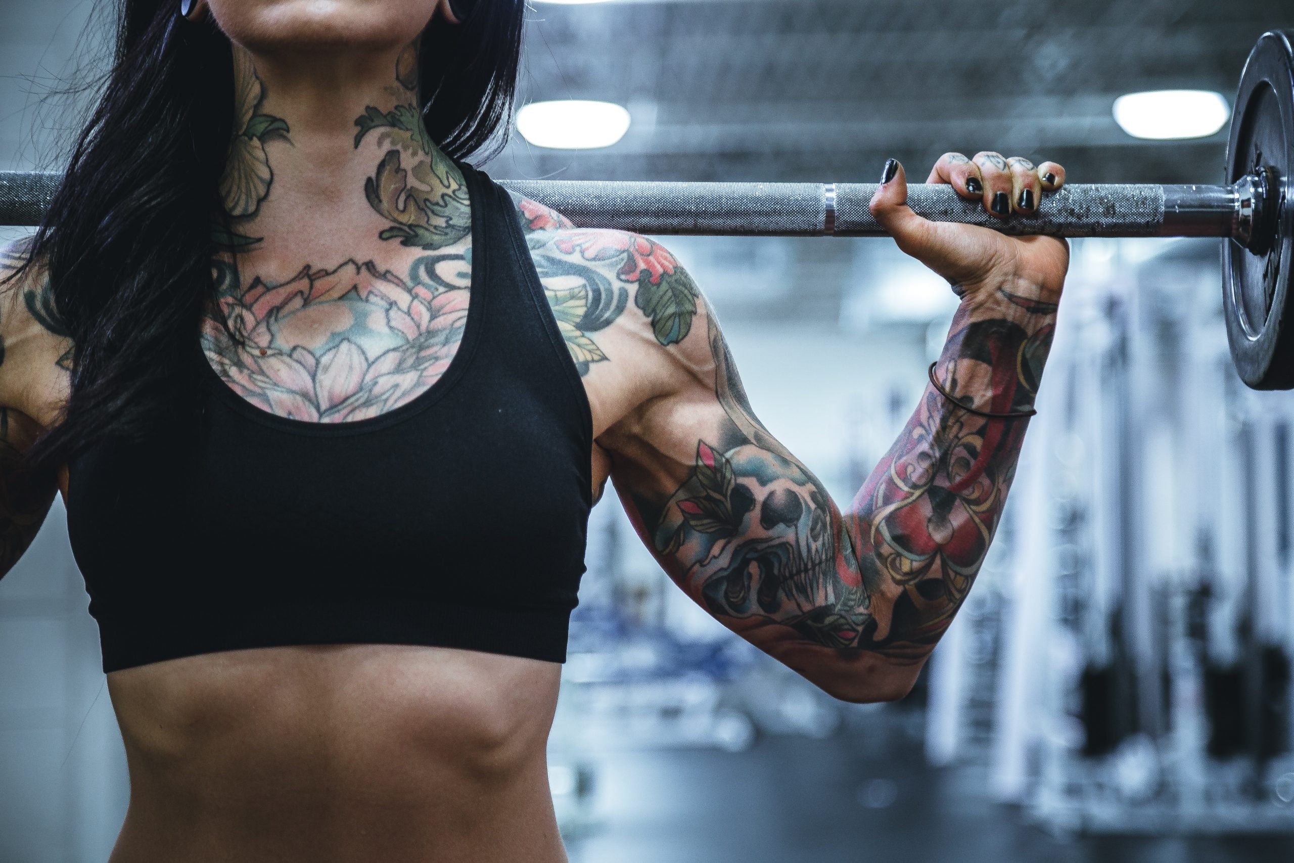 tattoed woman with weights rested across shoulders